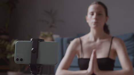 detail shot of a smartphone broadcasting through its camera the online yoga lesson of a young female influencer