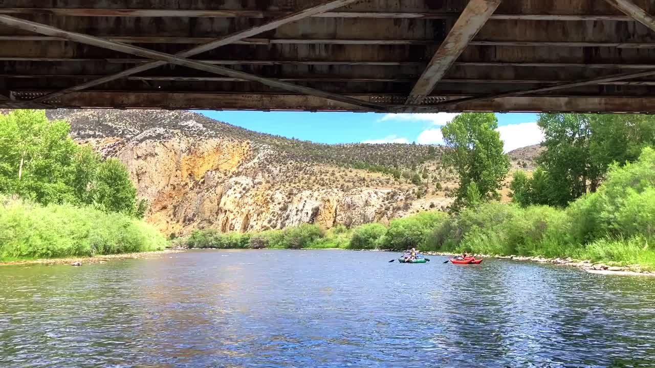 Scenery on the Big Hole river in Montana. Shot from a raft on the river going under a bridge. 2 people in the background floating on pontoons