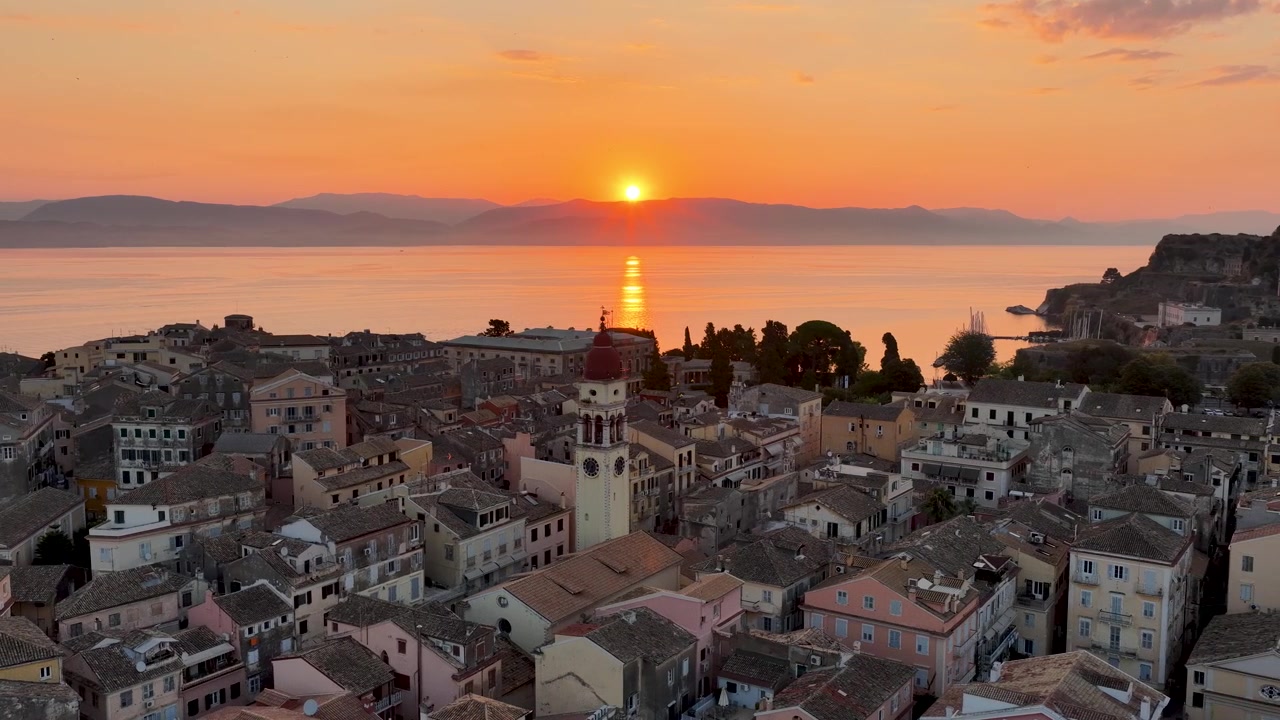 Maestoso panorama aereo di Corfù durante un'alba vibrante. Il sole splendente sorge sopra l'orizzonte, riflettendosi sul mare direttamente allineato con la prominente Chiesa di San Spiridione e i tetti della città