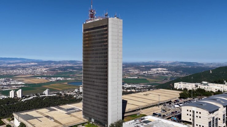 Ripresa con drone dall'alto che panoramica attorno all'edificio brutalista della Torre Eshkol, situato nel campus del Monte Carmelo e affacciato sul paesaggio sottostante in una giornata limpida