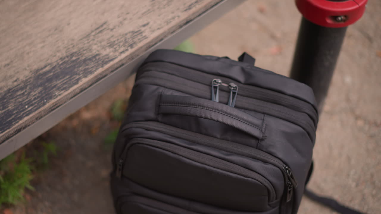 Uomo che esplora le tasche dello zaino, persona che fruga tra gli effetti personali in un ambiente urbano, figura maschile che cerca accuratamente negli scomparti dello zaino in un vivace parco con attività mirata