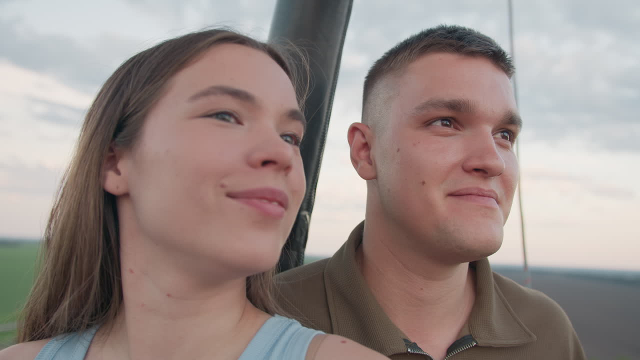 lady pointing out scenic countryside view to boyfriend as both smile inside colorful hot air balloon basket drifting serenely high above fields at golden hour capturing joyful adventurous moment