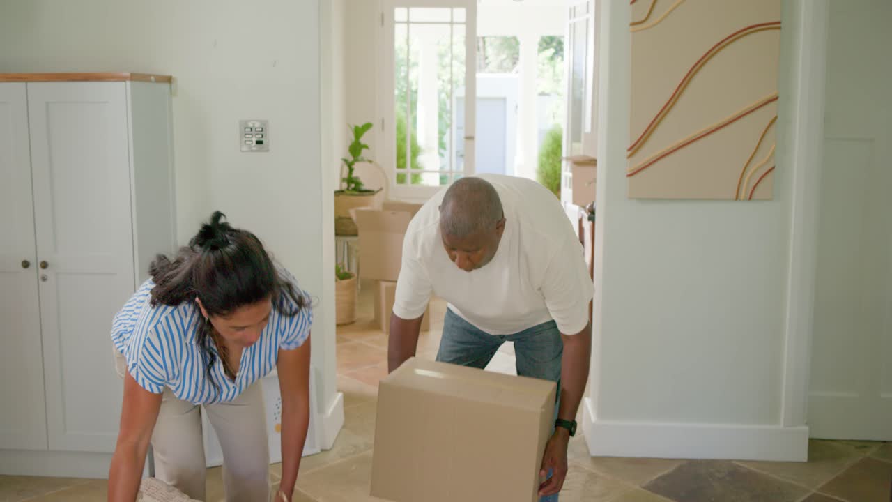 African American couple entering doorway carrying boxes, removing pillow, hugging, celebrating move