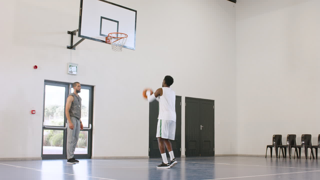 African american male basketball player catching, throwing basketball, male coach observing in gym