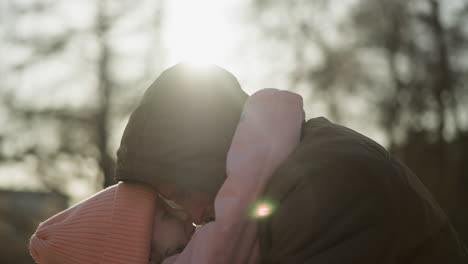 a little girl in a pink cap and jacket being carried by a man wearing a brown jacket, as they touch their foreheads together affectionately