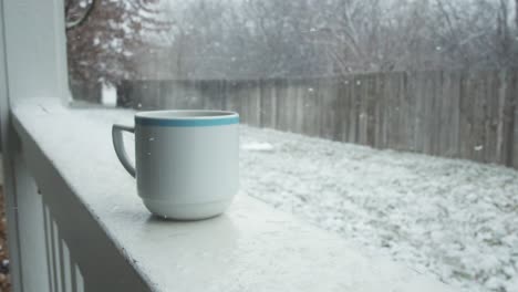 Una-Taza-De-Chocolate-Caliente-Descansa-En-La-Nieve-En-El-Porche-Del-Balcón,-Con-Vistas-Al-Patio-Trasero-De-La-Casa