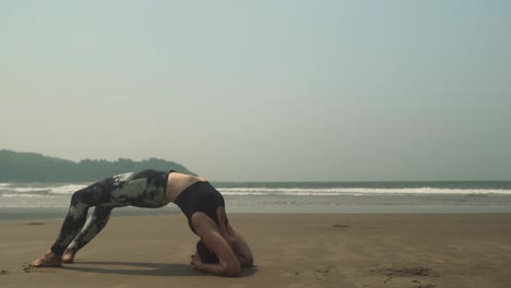 Beach-waves-washing-upon-shore,-fit-and-relax-girl-doing-yoga-stretch-on-shore