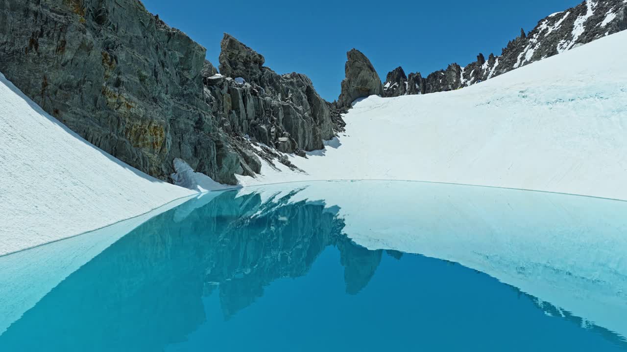 Křišťálově čisté modré alpské jezero obklopené sněhem a drsnými štíty v Chamonix ve Francii. Ideální pro témata cestování, zimy, přírody a dobrodružství, s kinematickým panoramatickým pohledem.