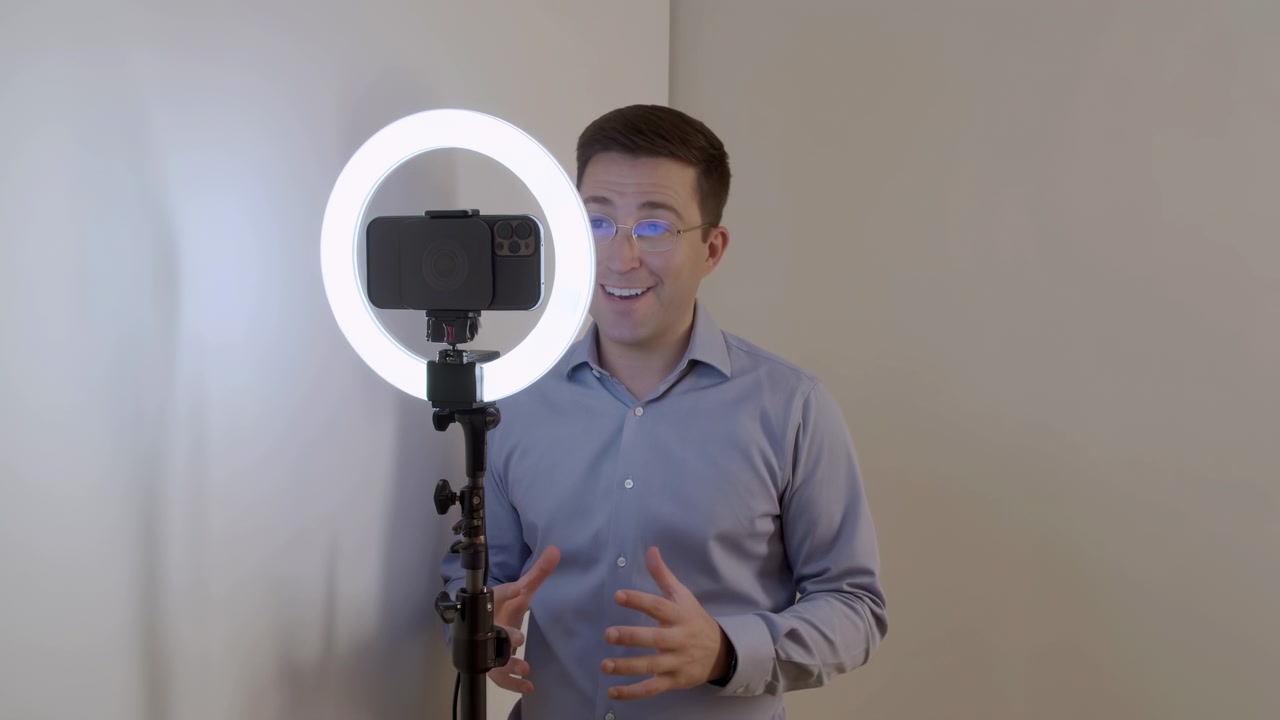 Presentatore caucasico registra tutorial con ring light, uomo caucasico in camicia blu che parla allo smartphone