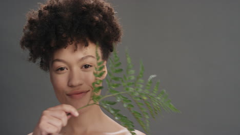 Retrato-Hermosa-Mujer-De-Raza-Mixta-Tocando-La-Cara-Con-Hojas-Acariciando-Una-Tez-De-Piel-Suave-Y-Saludable-Disfrutando-De-Una-Belleza-Natural-Juguetona-Sobre-Fondo-Gris