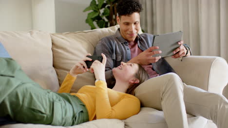 una pareja feliz sentada en el sofá usando un teléfono inteligente y una tableta en casa, en cámara lenta