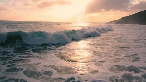 flying low over the crashing ocean waves at sunset