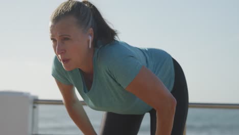mujer mayor tomando un descanso de correr en un paseo marítimo