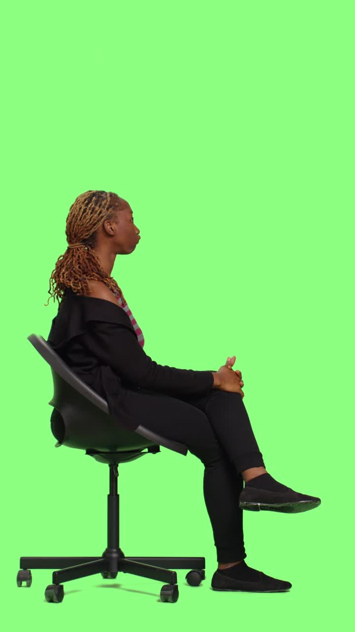 Video verticale: giovane seduto su una sedia che posa su uno sfondo con greenscreen