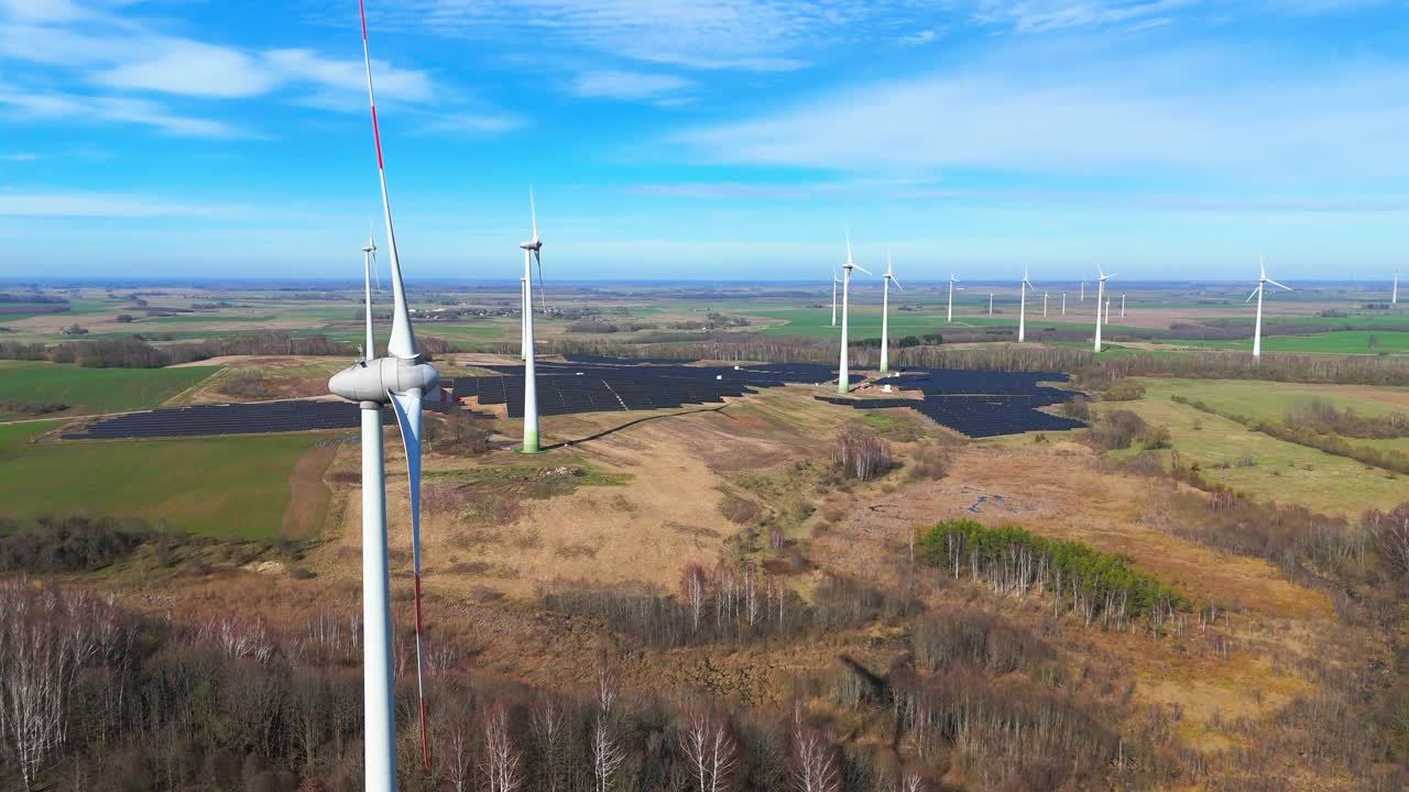 Aerial shot of large power plant of solar panels in Electrum solar park and wind turbines in a vast field on a sunny day in Taurage, Lithuania