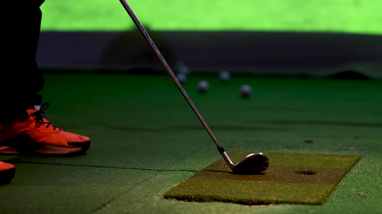 A low angle view of a golfer's orange shoes and club during indoor practice