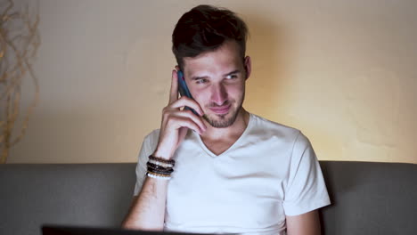 un joven con rastrojo y un peinado moderno, con una camiseta blanca, se sienta en casa, trabaja en su computadora portátil, intenta sin éxito llamar a alguien, habla solo, sacude la cabeza, estático 4k