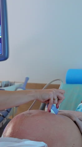 doctor checking up the baby development at ultrasound examination. obstetrician moves the equipment around big abdomen of a future mom. vertical video