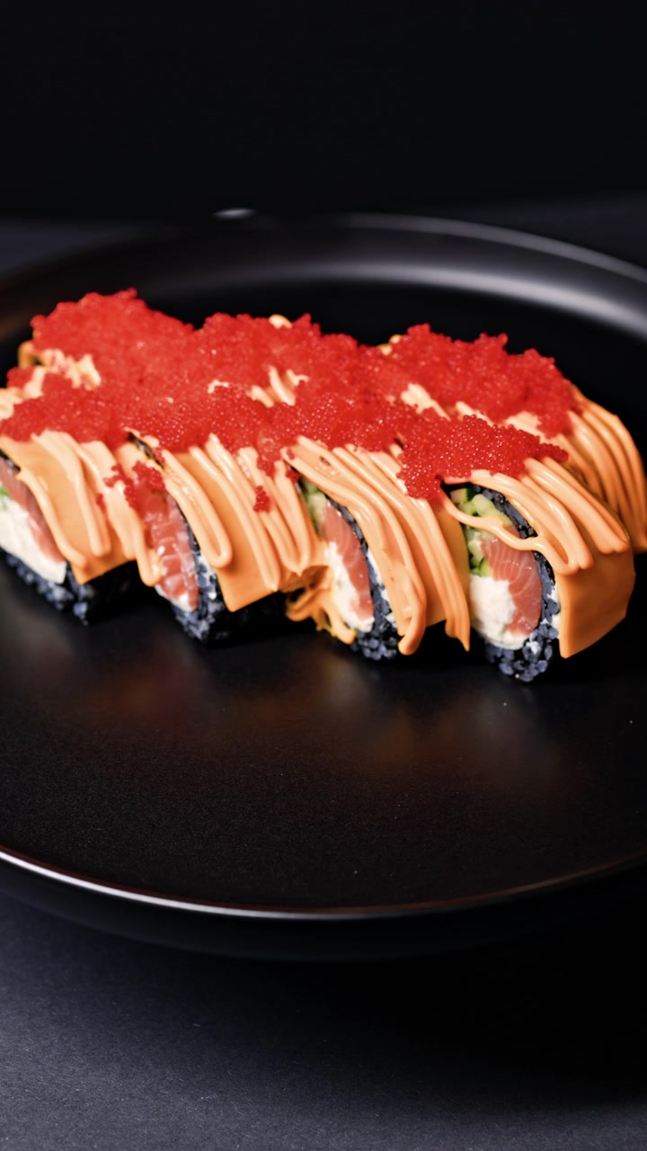 Sushi-Rollen werden auf einem schwarzen Teller mit bunten Belägen und einem dunklen Hintergrund serviert.