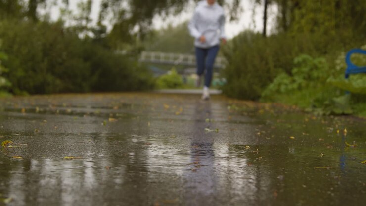 Primer plano desenfocado de mujer ejercitándose y manteniéndose en forma, corriendo bajo la lluvia hacia la cámara
