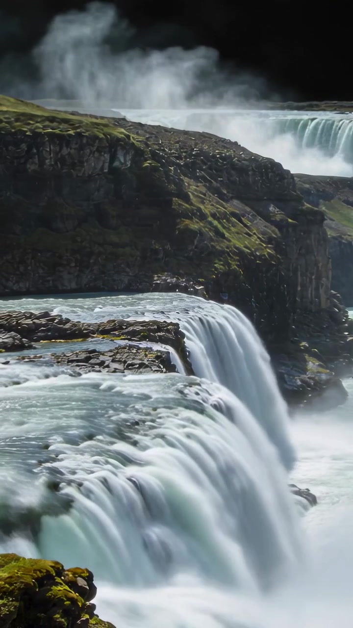 Video verticale: Fiume che straripa alimenta una cascata a più livelli su scogliere muschiose in una gola, creando nebbia