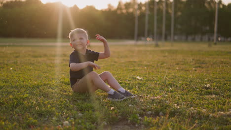 smiling boy waves off insects swarm on lawn at sunset