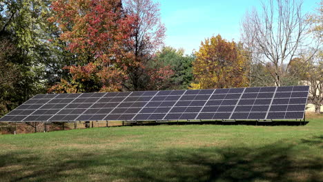 long-shot of solar panels on grassy lawn with autumn trees in background