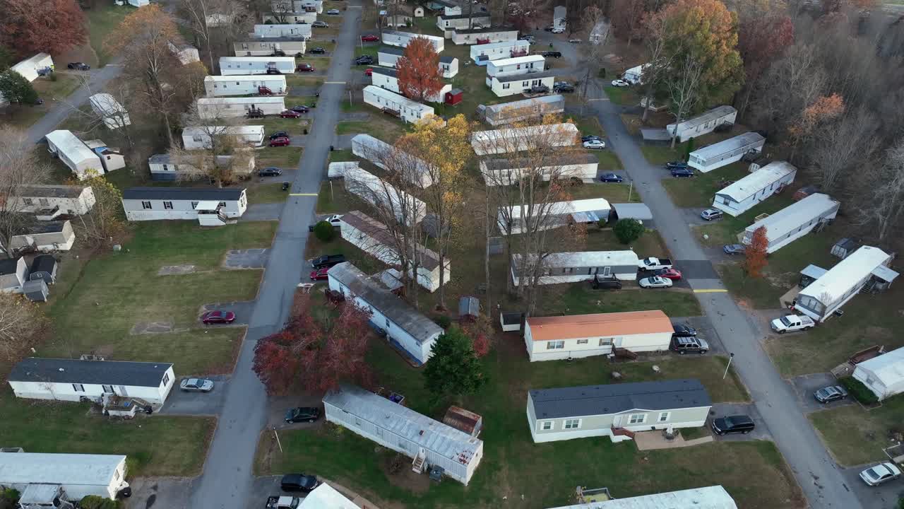 Drone flight over mobile trailer homes park with colored trees in fall. American suburb neighborhood with cheap homes and parking cars on driveway. Low housing area of Virginia, USA. Top down