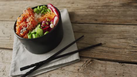 composition of bowl of rice, salmon and vegetables with chopsticks on wooden background