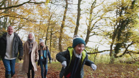 multi-generation family walks along path through autumn countryside with boy running ahead