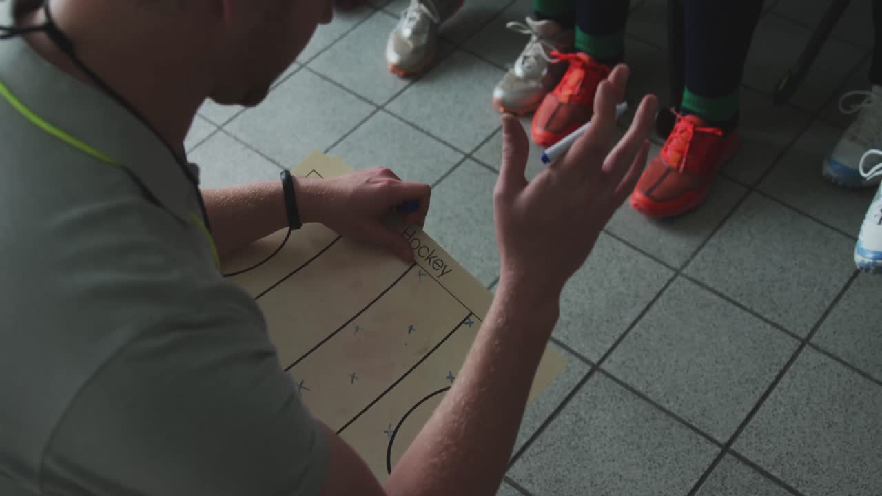 entrenador de hockey explicando el plan de juego con las jugadoras en el vestuario