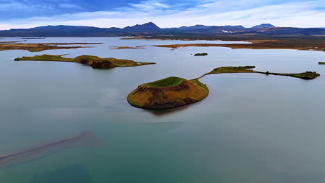 little islands covered with moss in the calm waterscape. large mountain range seen at backdrop. iceland scenery from top.