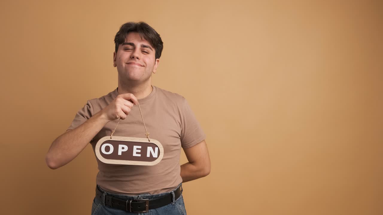 Smiling man with open sign inviting in beige studio