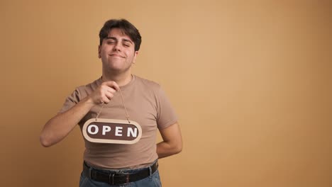 smiling man with open sign inviting in beige studio