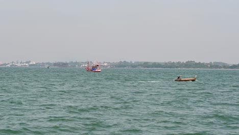 a brown small fishing boat going to the right while another is anchored as the city of pattaya is at the background, chonburi, thailand