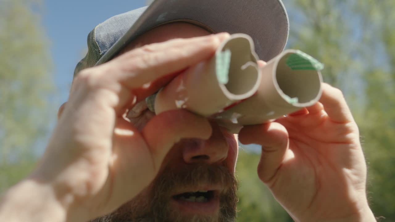 Eccentric caucasian man with beard looking through handmade cardboard binoculars
