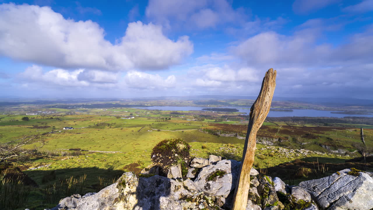 Timelapse panorâmico com efeito de movimento da paisagem rural com muro de pedra em primeiro plano, colinas e lago ao longe durante um dia ensolarado com nuvens, visto de Carrowkeel, no condado de Sligo, na Irlanda