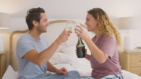 pareja enamorada con pijama en la cama en casa celebrando cumpleaños o aniversario con champán