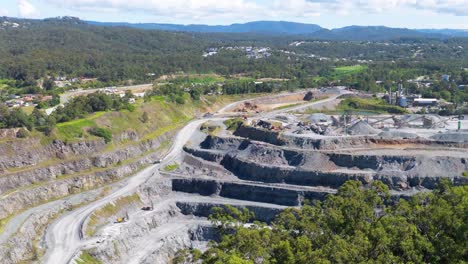 drone footage captures expansive quarry operations under bright daylight in gold coast, australia, highlighting terraced excavation and surrounding landscape