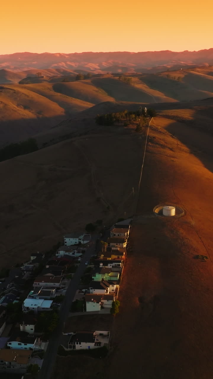 Lovely cozy city at the foot of the mountains. Stunning panorama of bare hills in the beams of setting sun. Aerial view. Vertical video