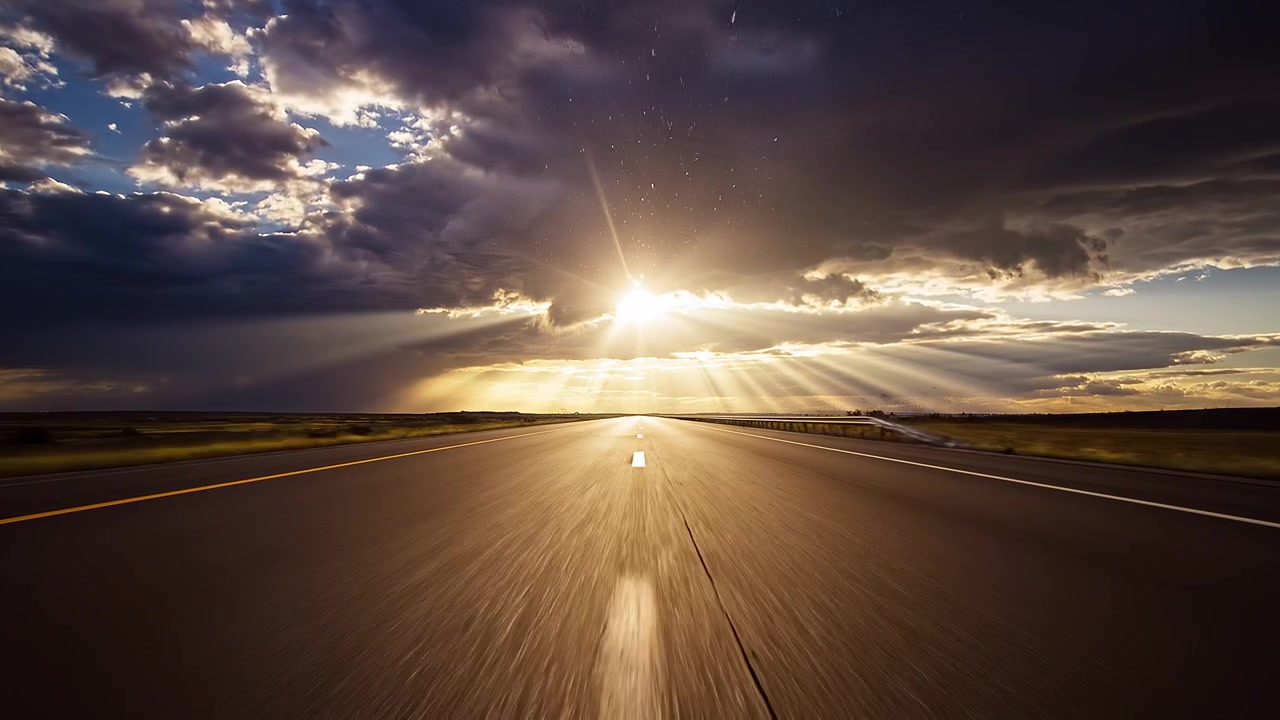Dramatic sunrays through storm clouds over an empty highway road