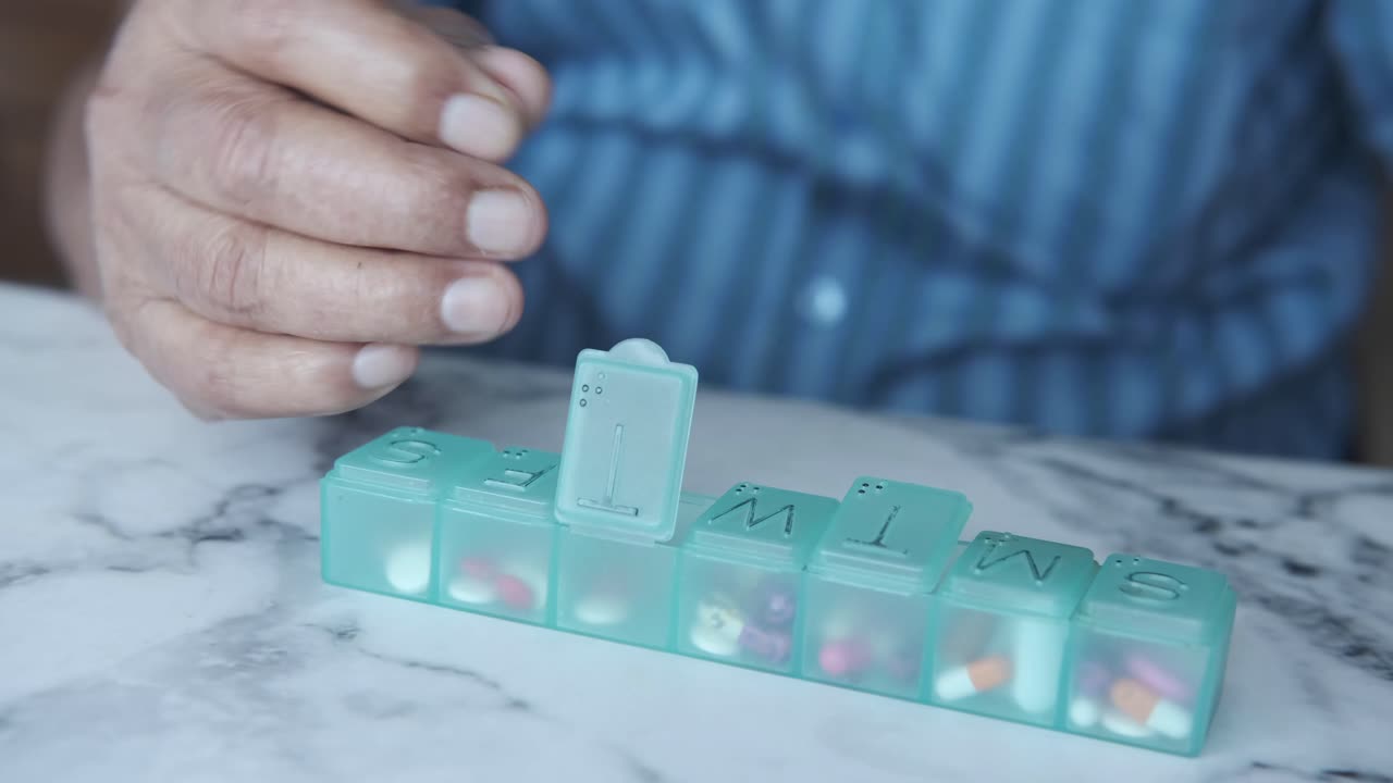 노인이 알약 조립기에서 약을 복용하고 있습니다.