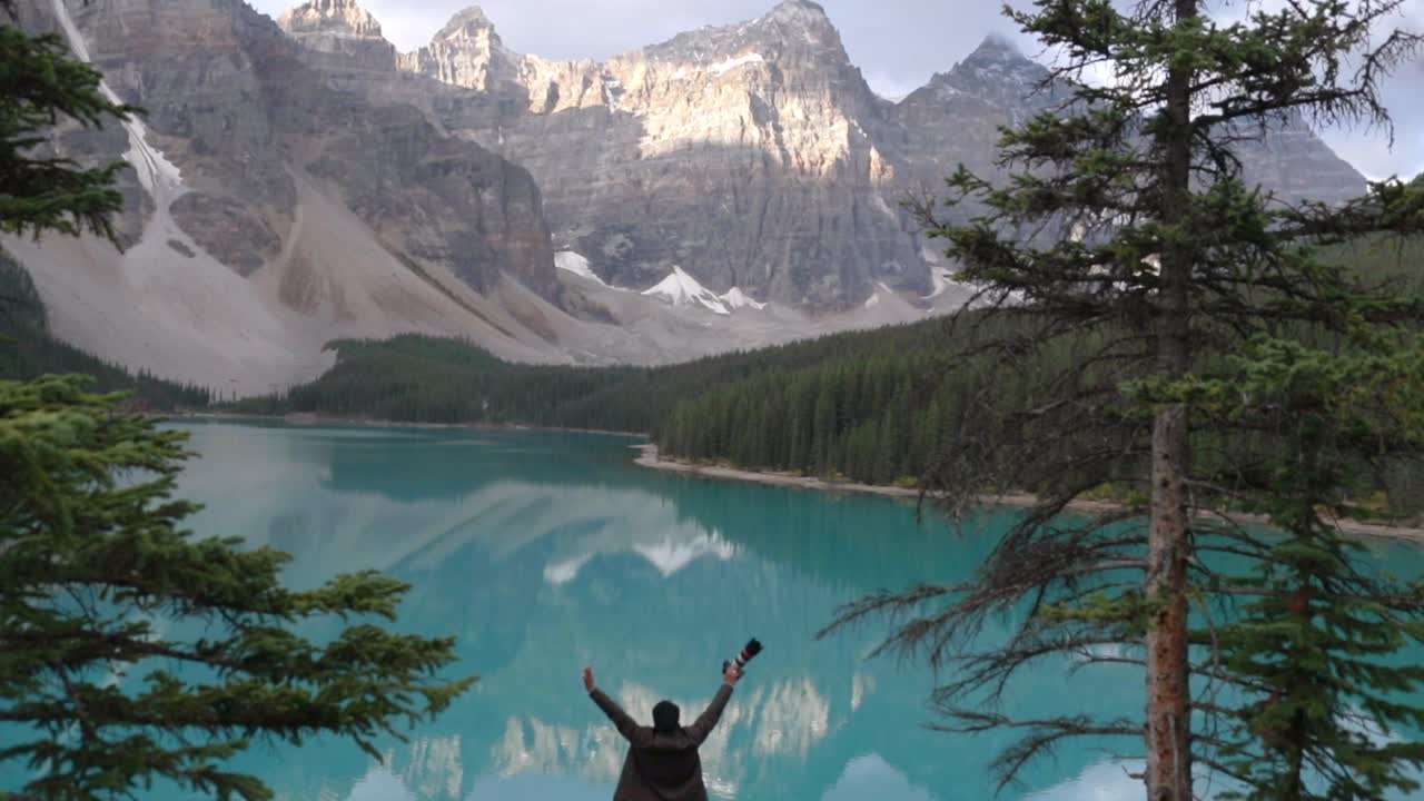 un fotógrafo de viajes feliz parado cerca de un lago de agua azul cerca de las montañas en banff, canadá