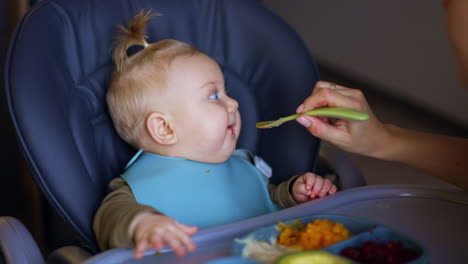 mother gives healthy food to her lovely baby. infant kid touches the food with his hand and looks surprised.