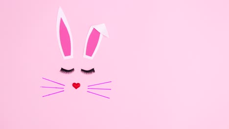 creative easter bunny with blinking lashes on pastel pink background. minimal flat lay stop motion