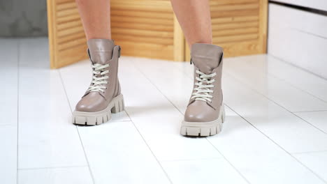 female model enters the shot wearing beige army boots with white laces. showing the stylish autumn footwear in studio backdrop.