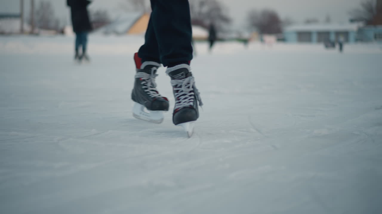 skillful skater gliding on ice rink near blurred people enjoying cold outdoor scene under pale winter sky, ice surface marked by skate blades reflecting soft light