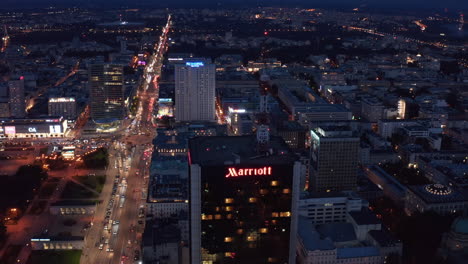 Imágenes-De-Diapositivas-Y-Panorámicas-Del-Alto-Y-Moderno-Rascacielos-Del-Hotel-Y-La-Concurrida-Calle-Que-Lo-Rodea.-Tráfico-Pesado-Por-La-Noche-En-El-Centro-De-La-Ciudad.-Varsovia,-Polonia