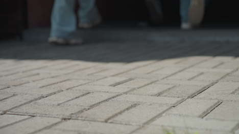legs in sneakers walking along interlocked pavement path under sunlight, creating dynamic shadows on ground, suggesting casual outdoor activity or journey on urban pedestrian walkway