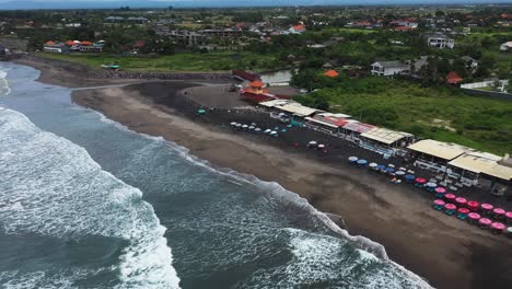 Playa-De-Pererenan-En-Bali,-Indonesia,-Con-Bares-De-Playa-Y-Cafés-Junto-A-Las-Olas-Del-Océano,-Muñeca-Aérea-En-Toma-De-Revelación